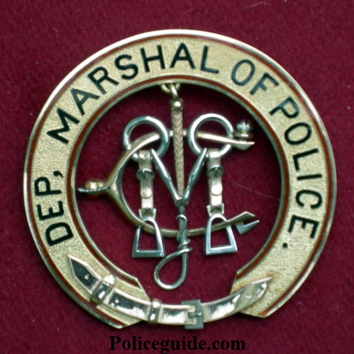 This elaborate and unique 14k gold suspension badge is in the form of a belt.  The wording Dep. Marshal of Police appears in hard black enamel.  The inner and outer borders are outlined in hard red enamel.  The emblem of the Maryland Jockey Club, in yellow and white gold, is suspended in the center.  The inscription on the reverse of the badge reads,  Jacob Frey From The Maryland Jockey Club / Spring Meeting 1882.  Frey was appointed to the Baltimore Police force with the rank of Captain in 1867, was made Deputy Marshal in 1870 and Marshal in 1885.  He served as Marshal (Chief of Police) until 1897.