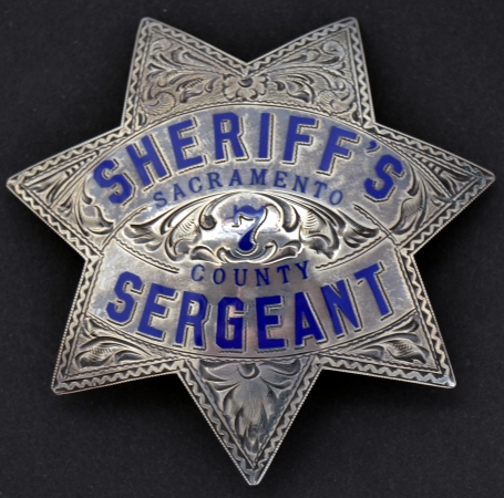 The original sterling sterling rank badges did not have an applied rank panel but were part of the blue enamel lettering on the badge.  To save money the department changed this policy in the 1950s and began adding an applied riveted panel to the top points.of a standard deputy sheriff badge.  This panel was also used on officers badges that worked as Constables in the Justice Courts.