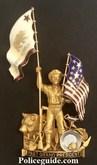 Presented to San Francisco Police Judge Matt Brady, this 1929 California NATIVE SONS OF THE GOLDEN WEST styled 14k solid gold figural badge: “GRAND PAST PRESIDENT.” These are extremely uncommon and were given out to special individuals within that group and rarely to others. The workmanship on this piece is superb with both the California Republic BEAR flag and the U.S. flag adorned with beautiful and detailed enameled work.  The theme of this piece is purely California depicting an imposing Figural GOLD MINER with his mining tools, next to an iconic California Grizzly Bear seated. Up against the miner is a gold pan with a natural native gold nugget.   The miner is gripping both flags in his two hands.  